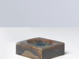 un petit cendrier carré en céramique posé sur une surface blanche