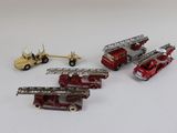 quatre camions de pompiers miniatures et un camion posés sur une surface blanche