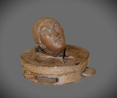 sculpture représentant une tête posée sur un socle en bois, sur fond gris