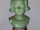 a small green bust of a child on a wooden stand