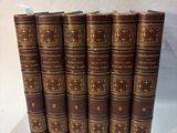 six old books lined up in a row on a white surface