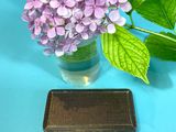 purple flowers in a vase and a small box on a blue surface