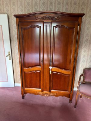 a wooden armoire in the corner of a room with a chair