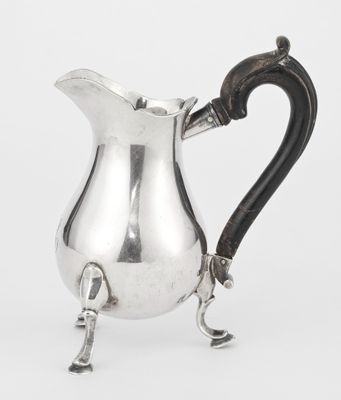 an antique silver pitcher with a black handle on a white background