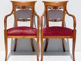 two wooden chairs with red velvet upholstered seats against a white wall