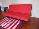 a futon bed with a red cover in a living room