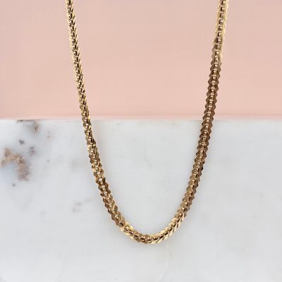 un collier à chaîne en or posé sur une surface en marbre