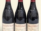 trois bouteilles de vin rouge sont alignées sur une surface blanche