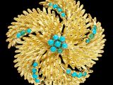 un gros plan d'une broche en or sertie de pierres turquoise