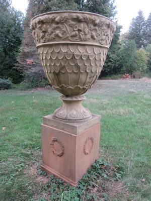 un grand vase en pierre posé sur un socle dans l'herbe