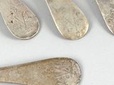 five silver spoons and a fork on a white surface