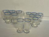 six verres transparents aux bords bleus sont alignés sur une surface blanche