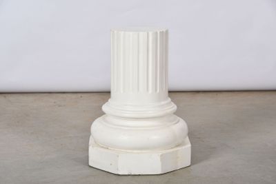 un pilier blanc avec un socle blanc posé sur un sol en ciment