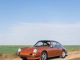 an orange car driving down a dirt road next to a green field