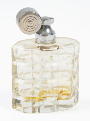 un flacon de parfum muni d'un bouchon métallique, posé sur une surface blanche