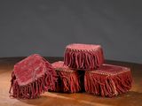 trois tabourets rouges à franges posés sur une table en bois