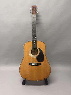 Une guitare acoustique est posée sur un support devant un fond blanc.