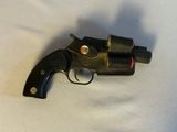 un pistolet noir posé sur une surface blanche, avec une lumière rouge