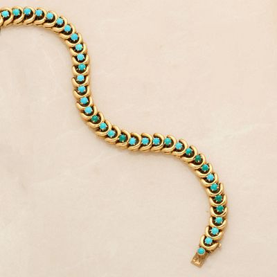a close up of a gold and turquoise bracelet on a white surface