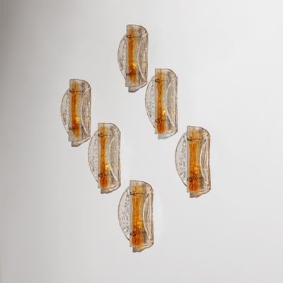 six appliques murales en verre sont disposées sur un mur blanc