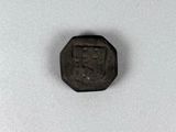 une vieille pièce de monnaie sur laquelle figure un petit visage, posée sur une surface blanche