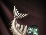 a silver fish statue with a green glass ball on a table