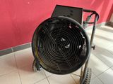 a black fan sitting on a cart in front of a red wall
