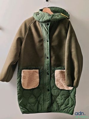 veste à capuche avec poches, suspendue à un cintre sur un mur blanc dans une pièce