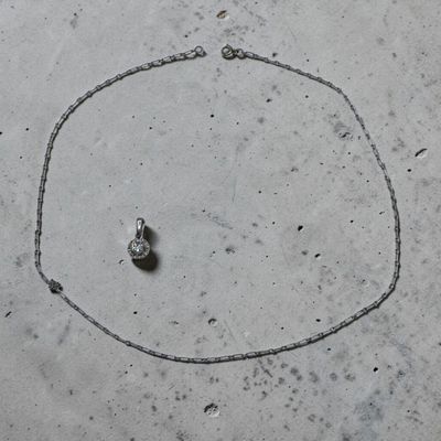 un collier en argent orné d'un diamant, posé sur une surface en béton