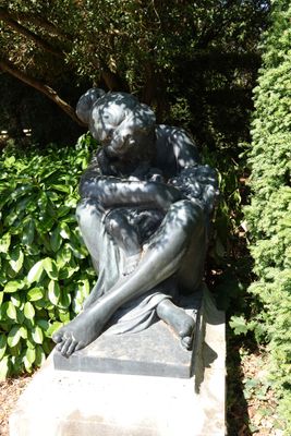 une statue représentant une femme assise sur un rocher dans un jardin