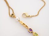 a close up of a gold necklace with a pearl and amethe