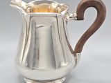 an antique silver pitcher with a wooden handle on a grey background