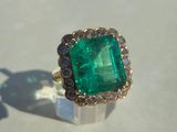 an image of a ring with a large emerald stone surrounded by small diamonds