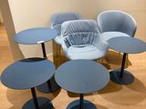 Plusieurs chaises et tables bleues sont disposées en cercle sur un parquet.