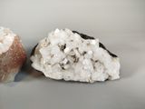 two pieces of rock with white crystals on a white surface