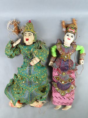 Deux petites poupées représentant des femmes en vêtements colorés sont disposées sur une surface grise.