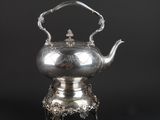 a silver tea kettle on a stand on a black background