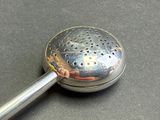 a metal strainer with a metal handle on a table