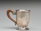 une coupe ancienne en argent, munie d'une poignée en bois, posée sur une surface blanche
