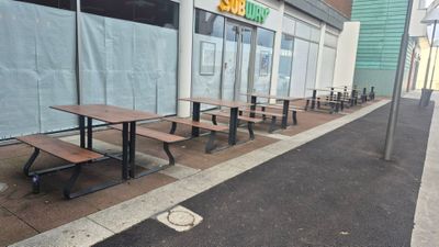 Des tables et des bancs sont alignés sur le trottoir devant un magasin.