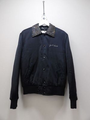 une veste noire avec un col et des poignets cloutés, suspendue à un cintre