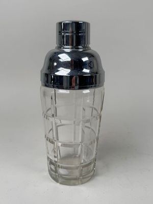 a glass shaker with a black lid on a white surface