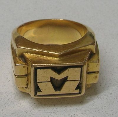 une bague en or sur laquelle est gravé un « M » en noir et blanc