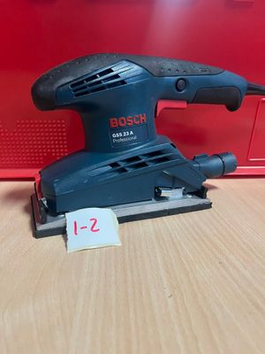 une ponceuse orbitale Bosch posée sur une table, à côté d'une boîte rouge