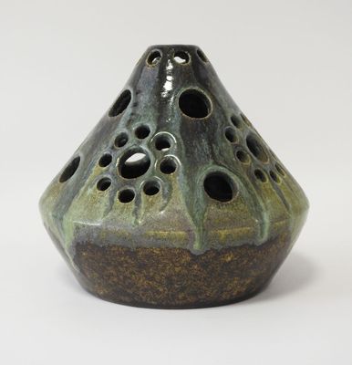 un vase vert percé de trous posé sur une surface blanche