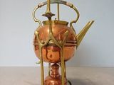 a copper teapot on a stand with a tea kettle on it