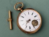 a gold pocket watch and a key on a green surface