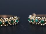 two gold rings with emeralds and diamonds on a black surface