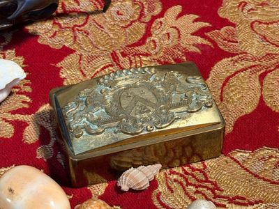 une boîte dorée posée sur un tapis rouge, entourée de coquillages