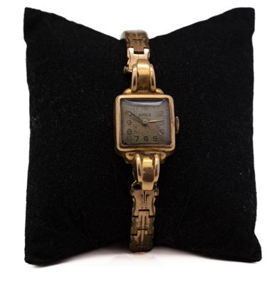 une image représentant une montre en or posée sur un coussin noir, sur fond blanc